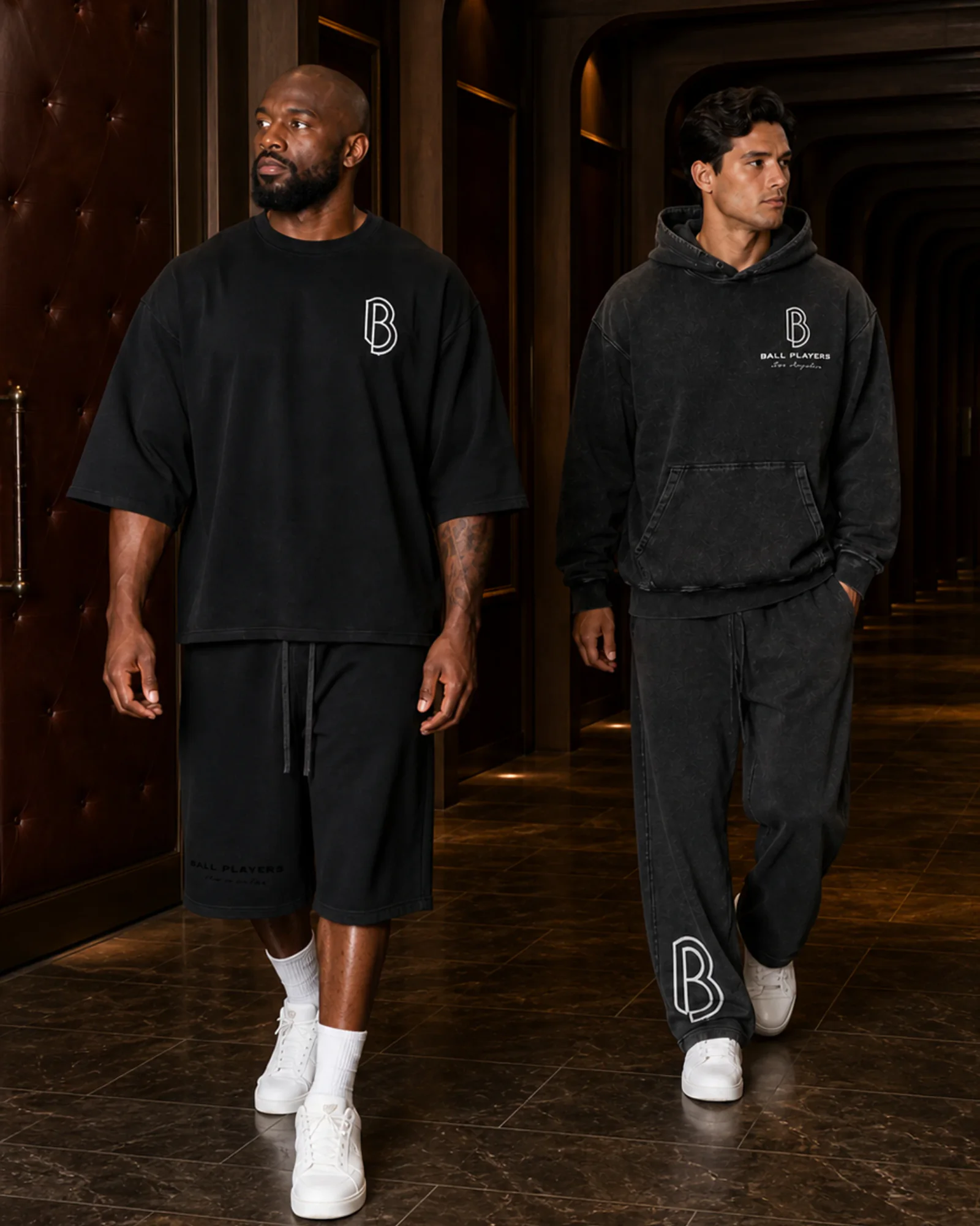 Two men wear Ball Players gym-streetwear while walking through a dark-wood athletic-club tunnel.